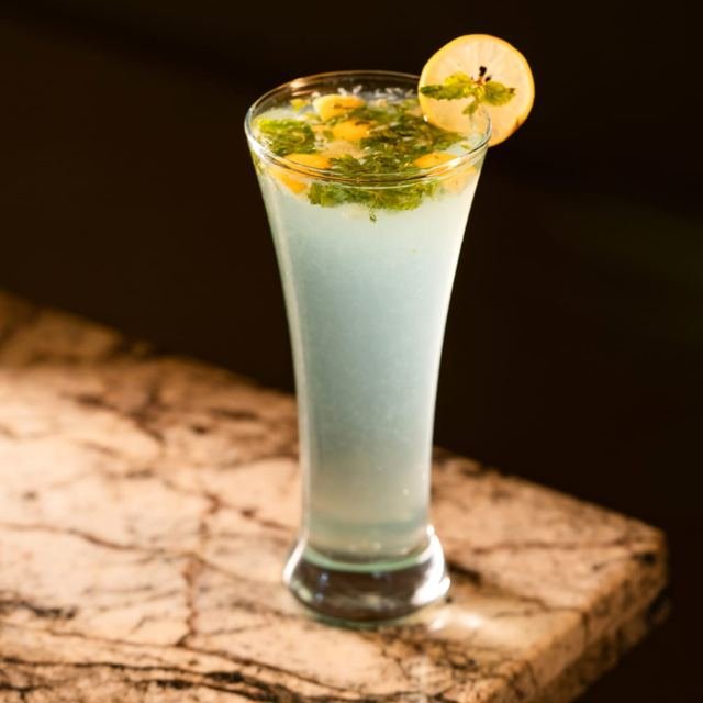 A tall glass of a chilled white cooler garnished with a lemon slice and mint.