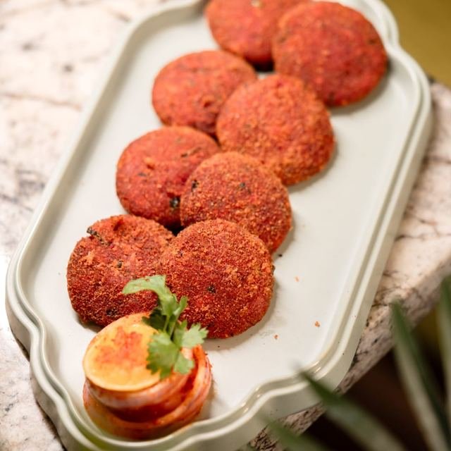 Crumb-coated round kebabs on a scalloped platter with a tomato and lemon garnish.