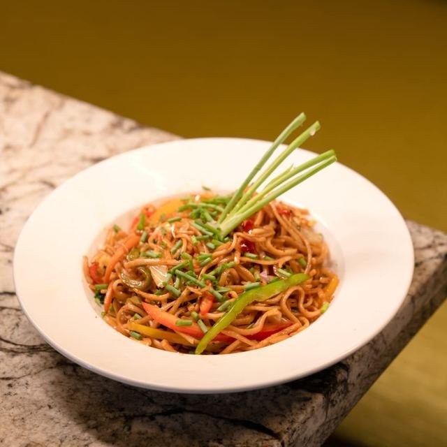Stir-fried noodles with vegetables and spring onion in a white bowl.