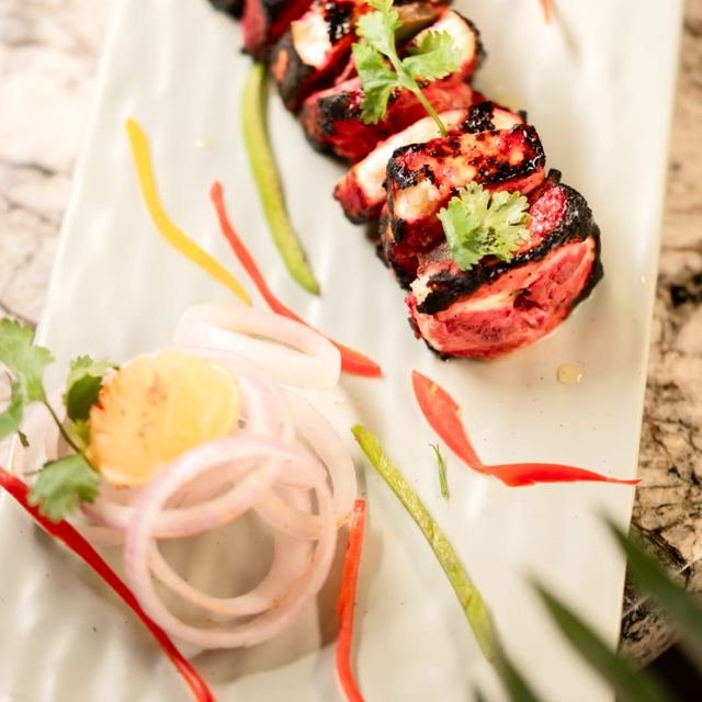 Red-marinated chargrilled pieces with coriander and onion rings on a long white platter.