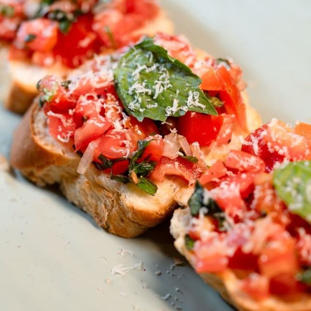 Toasted bread topped with chopped tomato, basil leaves and grated cheese.